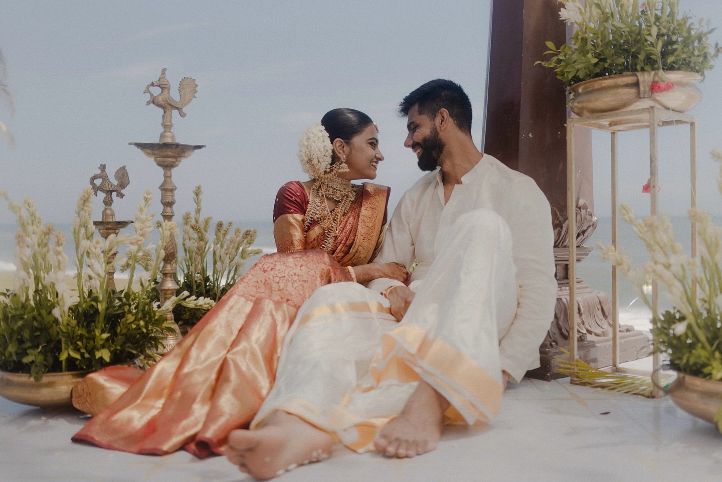 A newlywed couple seated together beside the sea